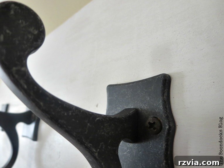 Close-up detail of a dark gunmetal double scroll hook on a white wooden coat rack, highlighting its elegant design and sturdy construction.