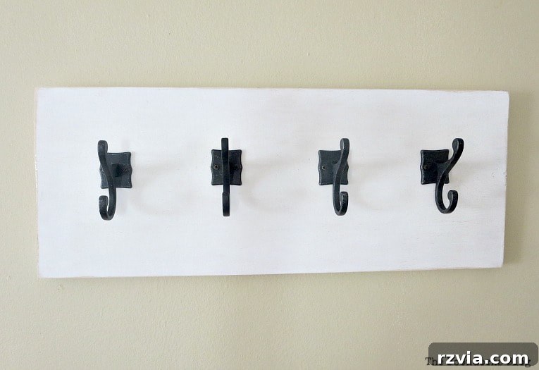 A completed white painted wooden wall hanger with dark gunmetal hooks, ready to be mounted and organize items in a stylish way.