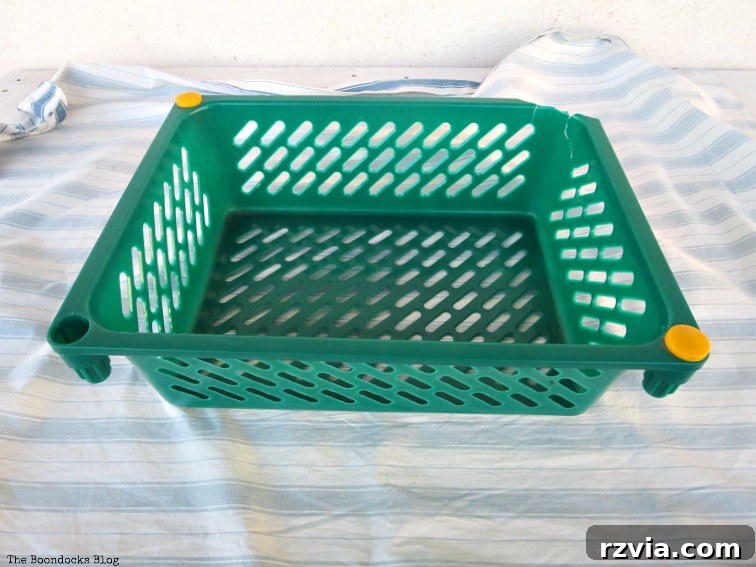 Fabric Fix: Giving New Life to Old Plastic Baskets 5 A green plastic basket centered on a large piece of blue and white striped fabric, illustrating the initial fabric placement.