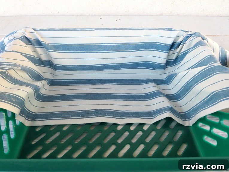 Fabric Fix: Giving New Life to Old Plastic Baskets 6 A person carefully folding one side of the blue and white striped fabric over the rim of a green plastic basket.