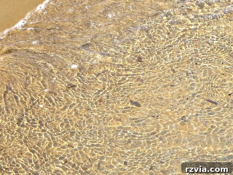 Kefalonia's Rugged Beauty: Where Brown Rocks Meet the Sea 9 Water reflects light, creating mosaic-like patterns in the sand, Kefalonia beach