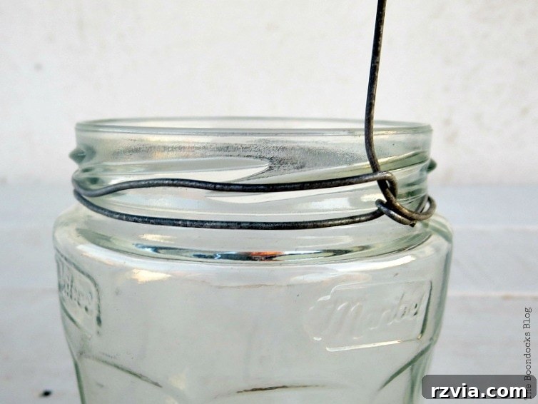 Transform Jars into Glowing Lanterns 11 A hand pulling the craft wire upwards through the loop to create a sturdy handle for the DIY jar lantern, showcasing the next step in the wire-wrapping process.