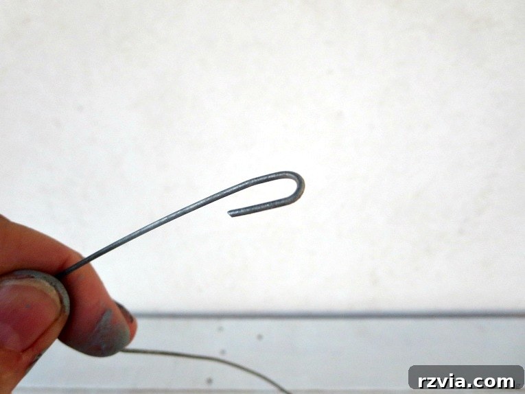 Transform Jars into Glowing Lanterns 6 A small, securely formed wire hook, demonstrating the initial stage of crafting a wire hanger for repurposed jar lanterns. Ignore the paint-splattered hands of a dedicated crafter.
