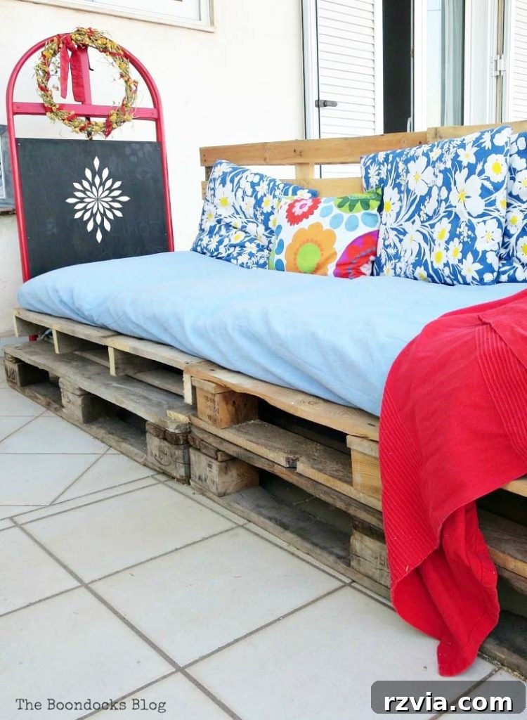 Super Simple Pallet Couch No Tools Needed 2 A completed DIY pallet couch covered with colorful cushions and blankets, showcasing an inviting outdoor seating area.