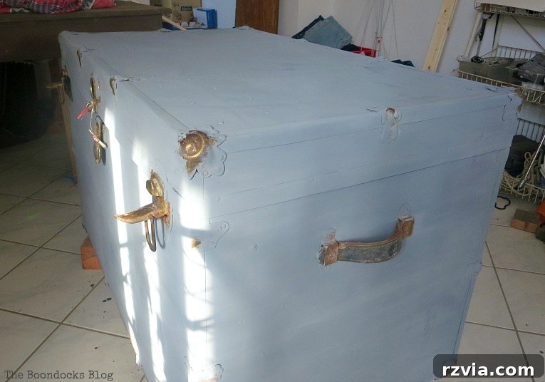 Aged to Perfection: Milk Painting a Vintage Metal Trunk 6 A person carefully applying a custom-mixed soft grey milk paint to the surface of a vintage metal trunk.