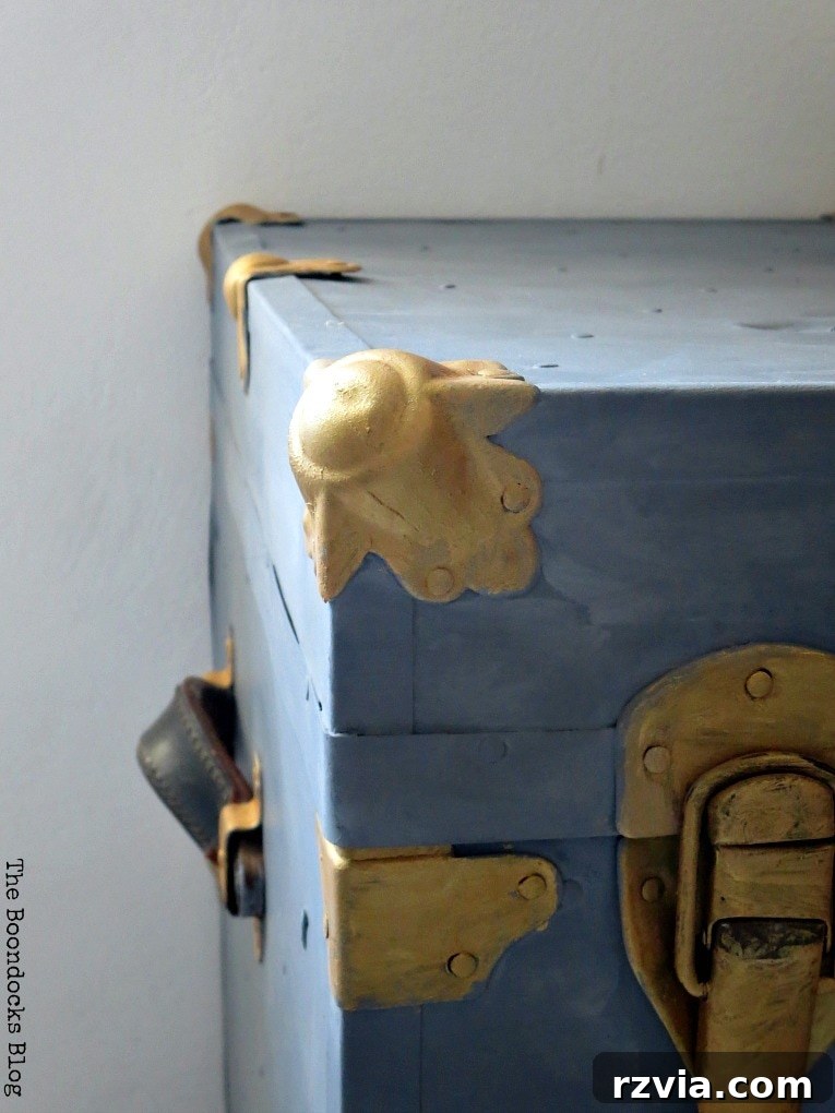 Aged to Perfection: Milk Painting a Vintage Metal Trunk 7 A hand applying beeswax finish to the freshly painted surface of a vintage metal trunk for protection and sheen.