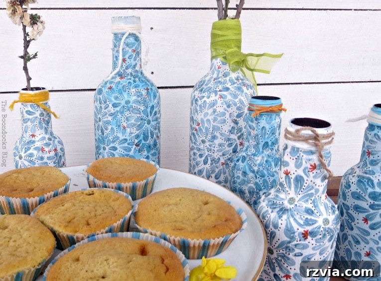 Finished decoupaged bottles next to cake stand with cupcakes, adding a delightful touch to the presentation.