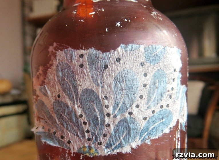 Close up of a decoupaged napkin on a brown plastic bottle, still showing the muddy color and wrinkles, highlighting the importance of priming and separating napkin plies.