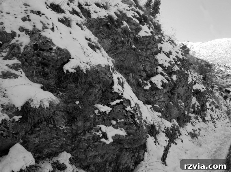 The White Crowns of Greece 13 Black and white image of a snow-covered mountain side with visible rocky outcrops, typical of the Greek mountainous terrain.