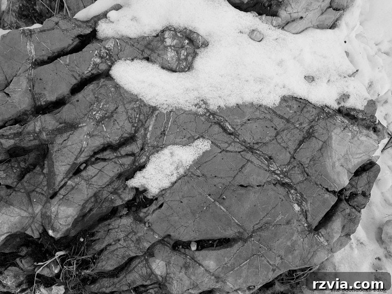 The White Crowns of Greece 17 A large boulder offering scenic views, surrounded by patches of snow in the Greek mountains, a perfect spot for reflection.