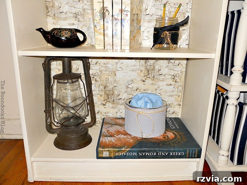 Paper and Paint Power: Bookcase Transformations 14 Bottom of the bookshelf decorated with a vintage gas lamp, books, milk pourer, and glass jar.