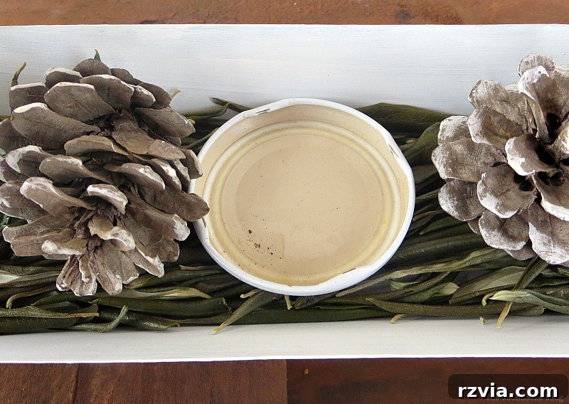 A jar lid positioned inside the chicken feeder to serve as a stable base for the candle, surrounded by pinecones for a DIY Christmas centerpiece. Illustrates a practical design tip. Photo by www.theboondocksblog.com