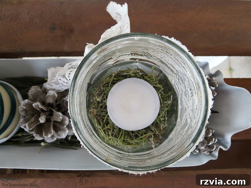 Overhead view of a jar with a white tea light and rosemary, showcasing the green and white color scheme and natural elements of the Christmas centerpiece. Photo by www.theboondocksblog.com