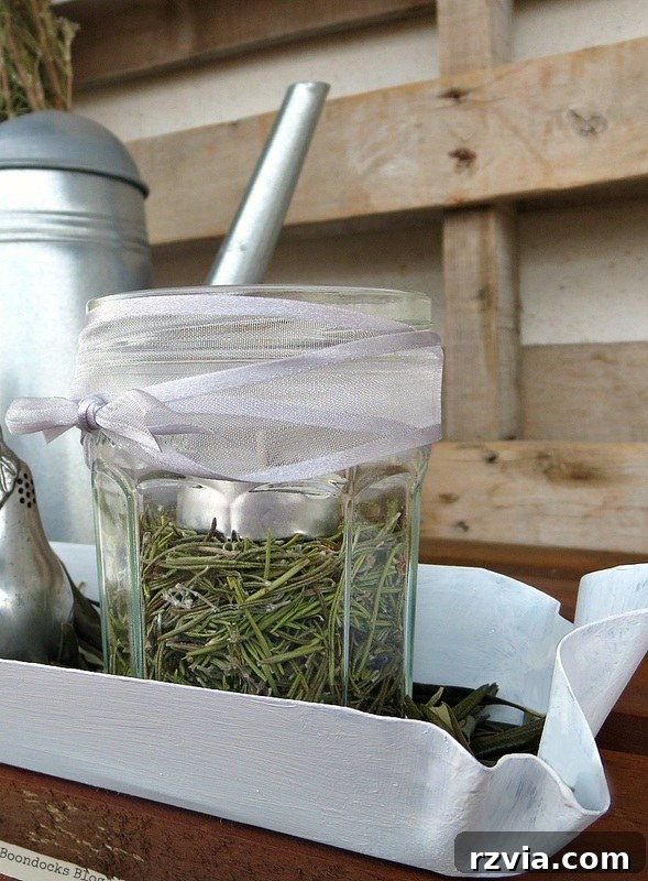 Detail shot of a jar with a white tea light and rosemary, adorned with a grey ribbon, showcasing the natural and refined elements of the second Christmas centerpiece design. Photo by www.theboondocksblog.com