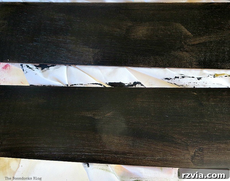 Applying the first coat of black chalkboard paint to a thin wood piece, transforming it into a DIY holiday sign base.
