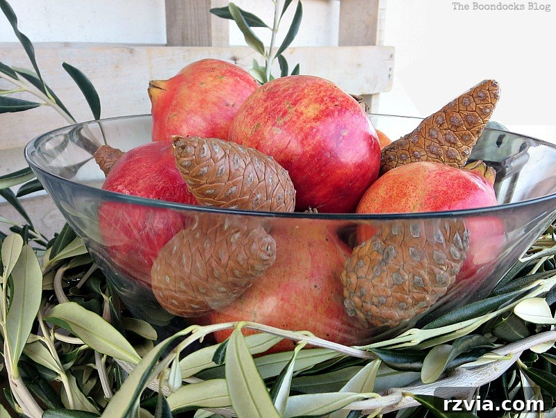 Autumn's Bounty for Your Table 9 Glass bowl centerpiece showcasing a harmonious mix of rich red pomegranates and varied pinecones, all artfully arranged within a circle of fresh olive branches.