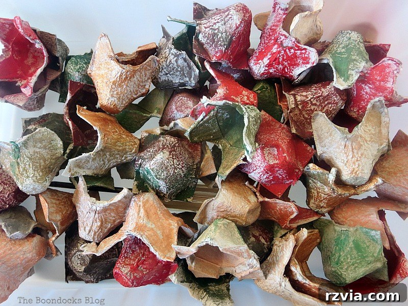 Several egg carton cups painted in warm fall colors, drying on a surface, showcasing the vibrant palette for upcycled fall flower decor.