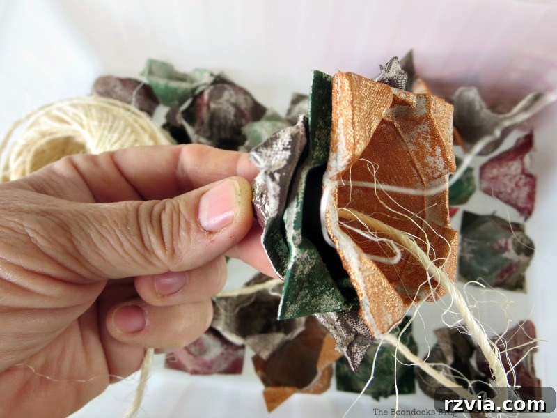 Twine threaded through three layered egg carton cups, twisted to form a natural flower shape, illustrating the assembly of DIY fall flowers.
