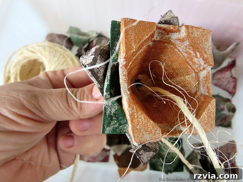 Detailed view of three egg carton cups threaded on twine, showing the twisted and uneven layering that creates a multi-petaled floral effect for the fall decor.