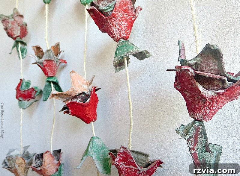 Strings of egg carton flowers and painted half-shells (leaves) hanging, ready to be attached to a piece of wood for a complete fall decoration.