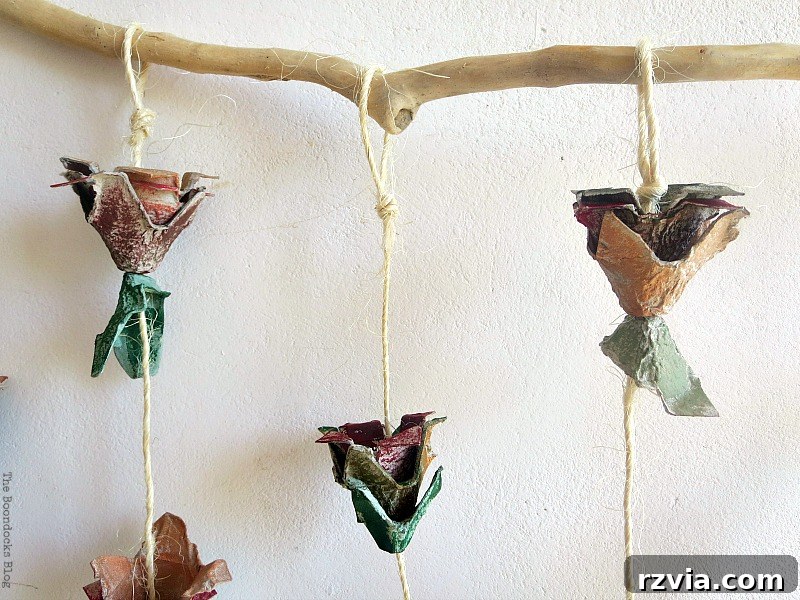 Close-up of egg carton flower strings being tied to a rustic piece of wood, showing the final assembly step for the DIY wall hanging.
