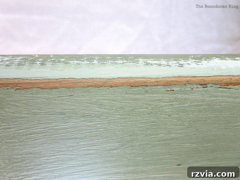 The process of distressing the freshly painted bed frame, revealing layers of green and the original wood for an aged, vintage look.