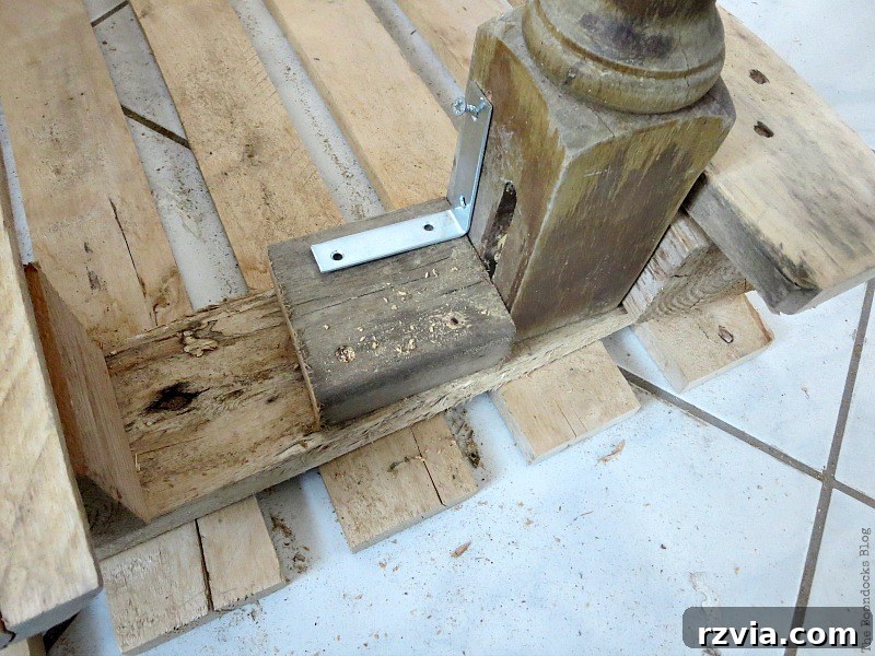 Upcycled Elegance: Crafting a Pallet and Salvaged Wood Table 6 Close-up view of the brackets and an additional piece of wood used to securely attach the reclaimed legs to the pallet, reinforcing the DIY table's stability. www.theboondocksblog.com
