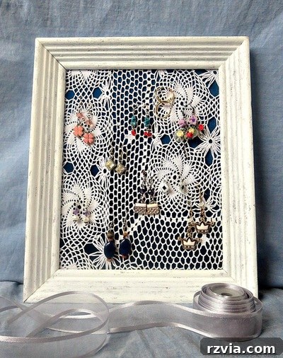 DIY Earring Storage Made Simple 2 A beautifully crafted DIY earring organizer featuring a white painted frame, a blue satin fabric background, and a delicate white doily for hanging earrings.