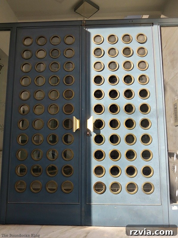 Contemporary metal door with decorative circular elements, showcasing a blend of strength and artistry in Greece, by www.theboondocksblog.com.