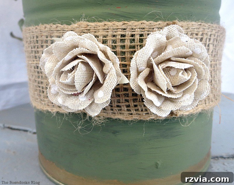 Fabric flowers being added as a decorative touch to the DIY repurposed tin can vase, completing the design.