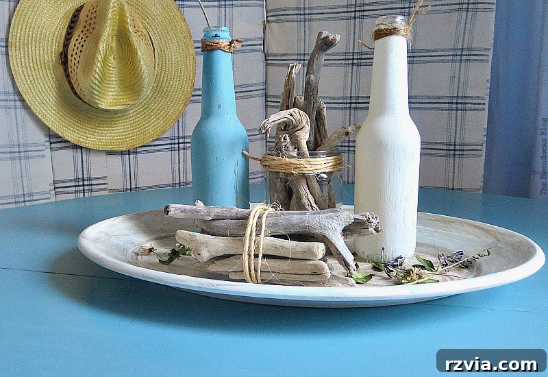 A curated beachy vignette on the newly finished Greek Beach Table, featuring painted bottles and driftwood, capturing the coastal essence for the Int'l Bloggers Club Challenge, by theboodocksblog.com