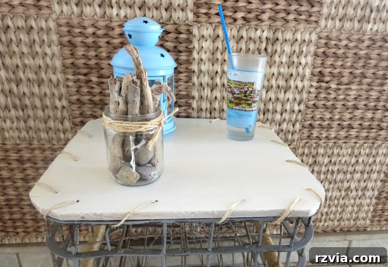 Beyond the Box: Milk Crate Table Reinvention 10 Close up of the white painted top of the table adorned with a drinking cup, a vibrant blue lantern, and a jar containing decorative driftwood, highlighting the crisp new finish.