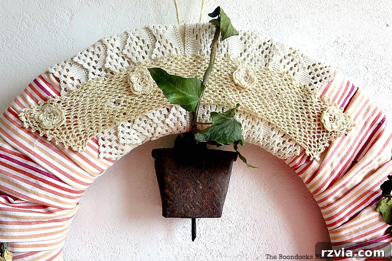 Detailed shot of crocheted elements and an antique bell integrated into a spring wreath, showcasing rustic and handmade embellishments.