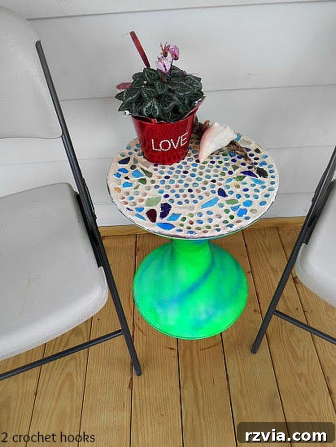 Craft Your Own Sea Glass Mosaic Table 12 The fully assembled sea glass mosaic table, adorned with its new top, positioned gracefully next to two folding chairs on a cozy porch setting, reflecting its potential as outdoor decor.