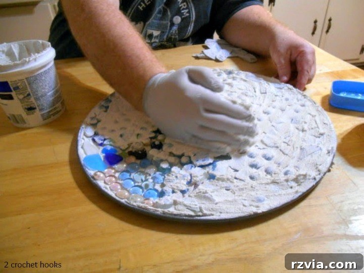 Craft Your Own Sea Glass Mosaic Table 8 An additional layer of grout being carefully spread over the sea glass and marbles, ensuring all gaps and crevices are filled for a secure and smooth finish.