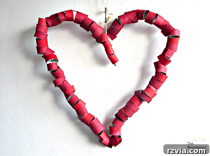 The heart-shaped wire frame progressively covered with sections of red-painted toilet paper rolls, creating a textured wreath.