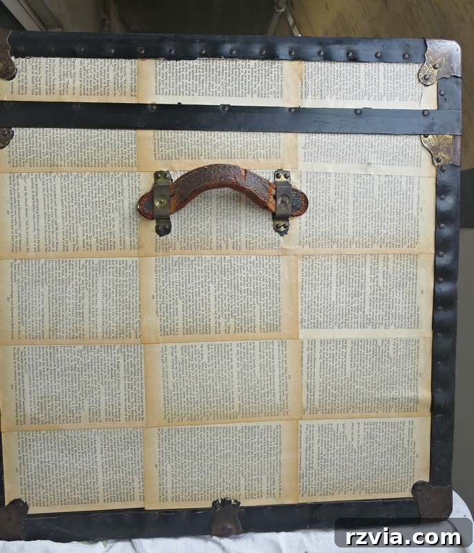 Side view of the old trunk fully covered in vintage book pages, showcasing the ongoing transformation